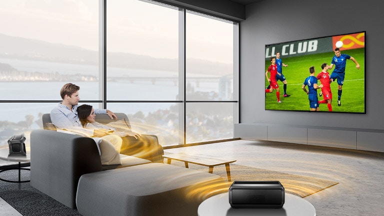 رجل وامرأة يشاهدان لعبة رياضية على شاشة التلفزيون في غرفة المعيشة مع مكبرات صوت خلفية بلوتوث