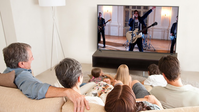 أسرة تتكون من سبعة أفراد تجمعوا في غرفة المعيشة لمشاهدة أحد الأفلام. شاشة تلفزيونية تظهر فرقة خلال أدائها أحد العروض.