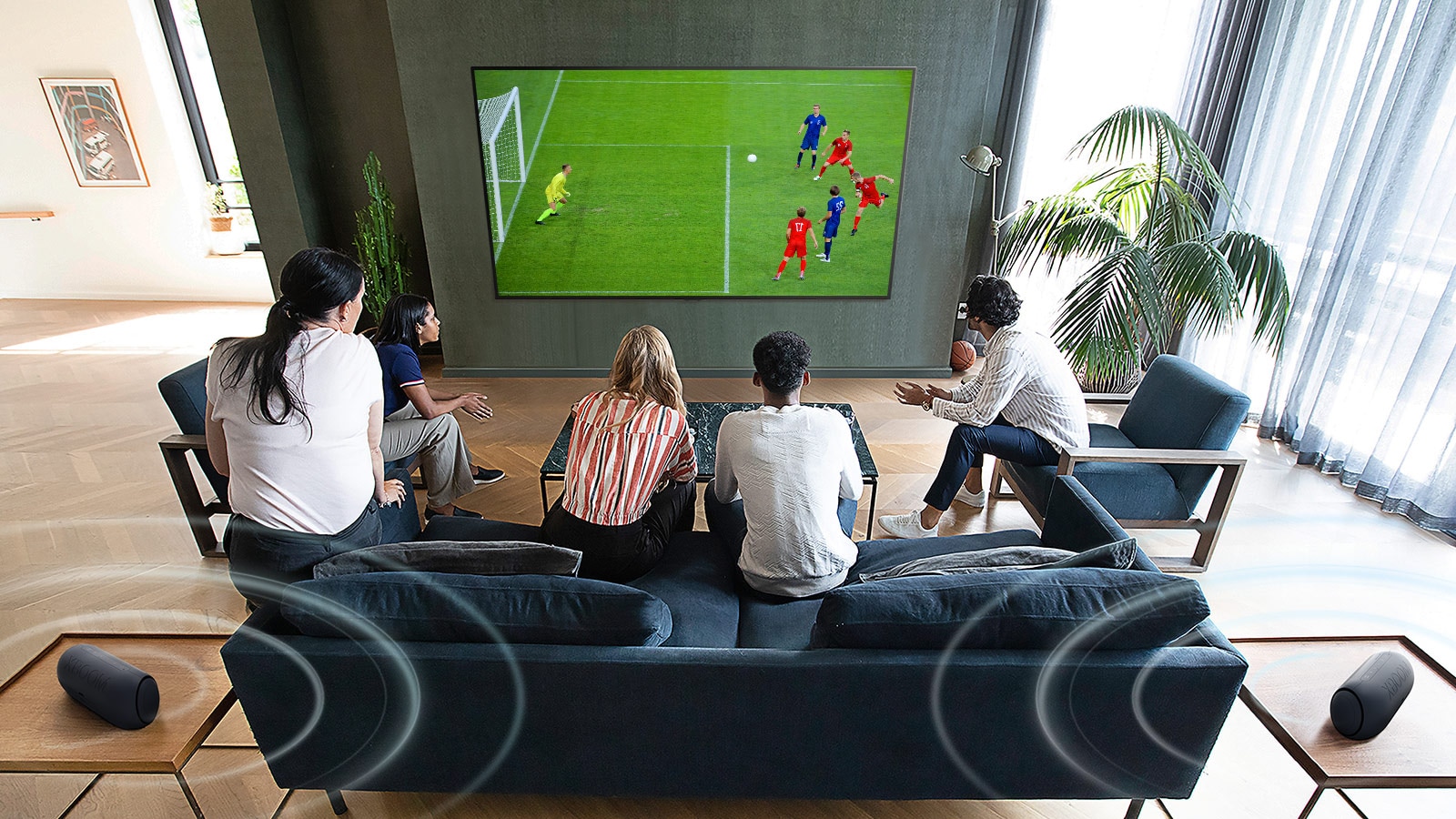 خمسة أشخاص مجتمعون أمام شاشة تلفاز مسطحة مثبتة على الحائط لمشاهدة مباراة كرة القدم. 
