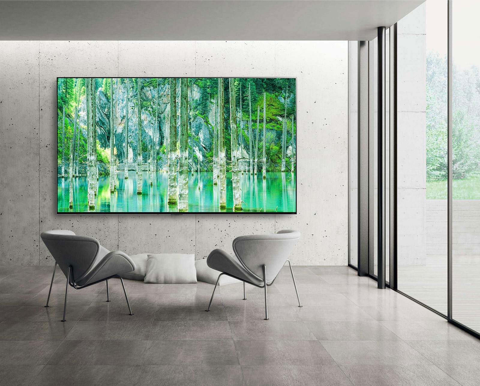 صورة توضح شاشة تلفزيون QNED MiniLED كبيرة الحجم من إل جي مثبتة على جدار رمادي من الخرسانة المجردة. شاشة تعرض مشهدًا طبيعيًا أخضر اللون مع وجود كرسيين أمام التلفزيون.