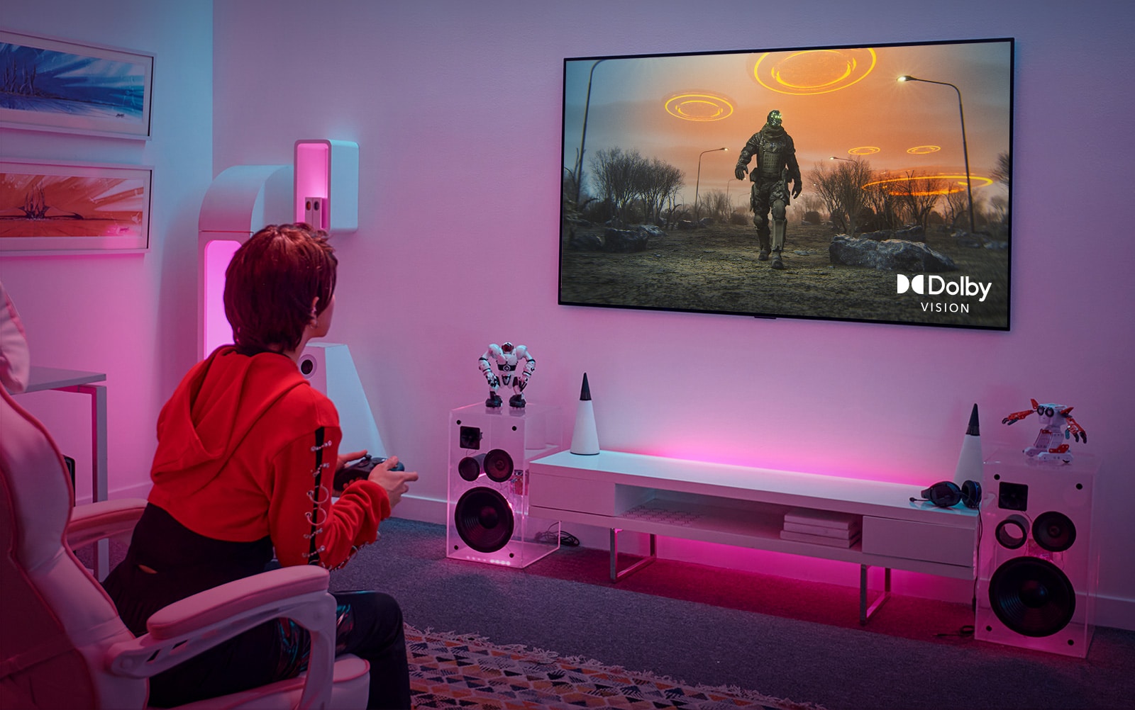 صورة توضح فتاة تلعب لعبة تقمص الأدوار بجهاز تحكم وشاشة تلفزيون كبيرة معلقة على الجدار في غرفتها الوردية.