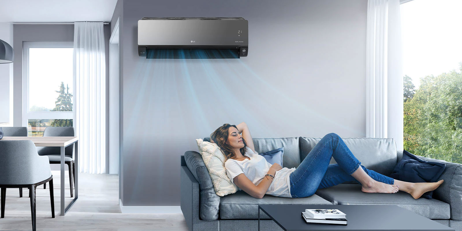 A woman lounges on a couch in a living room with the LG air conditioner installed above her on the wall. Blue streams of air are on the image to indicate it is on and cooling the room.