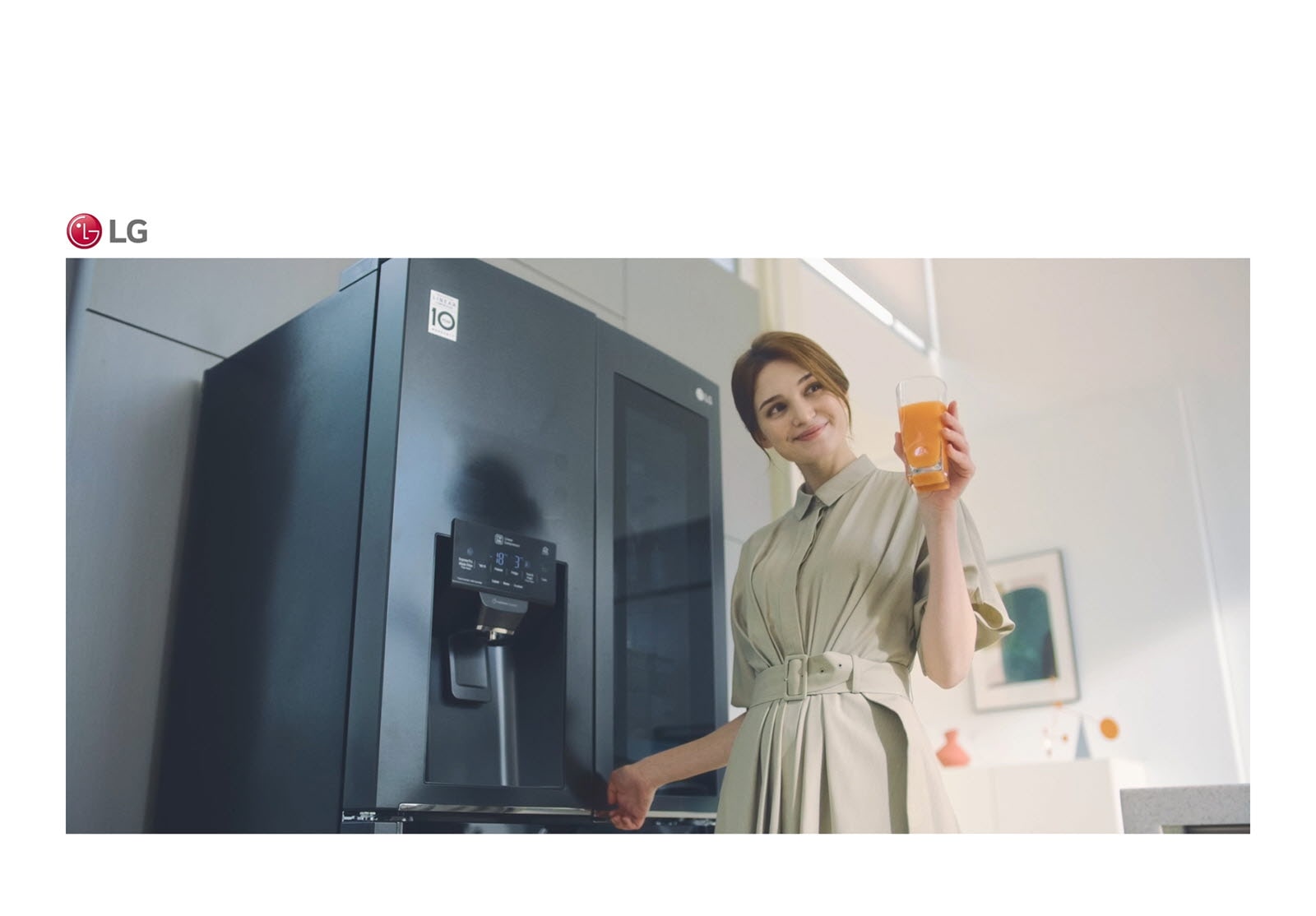 A woman stands in front of the refrigerator holding a glass of juice and smiling as she closes the door.