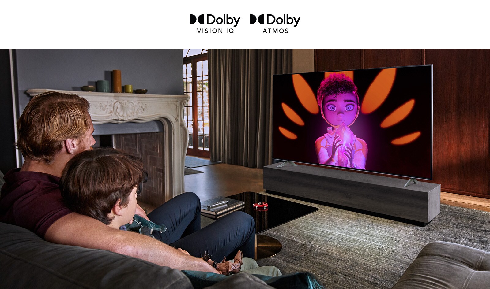 A man and boy sat side-by-side on a sofa watching a movie on a large flatscreen TV. The screen shows an animated character against a black background.