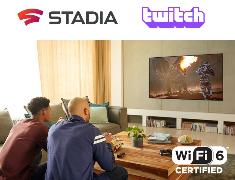 The logo of Google Stadia and Twitch are in a line. Two men sitting on the sofa are playing game with controllers and Wi-Fi 6 certified in a living room.