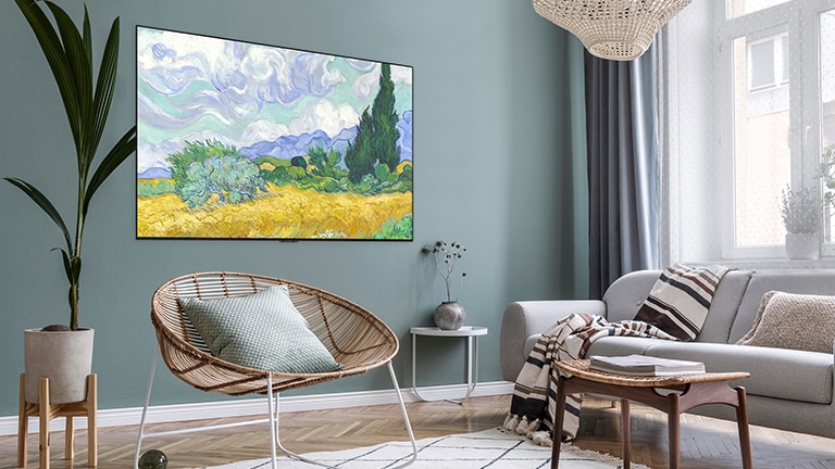 A TV displaying an art is hung on the green wall in a living room with a chair, a sofa, and a flowerpot.