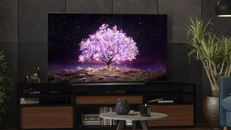 A TV displaying a shining pick tree in the middle is in a dark living room.
