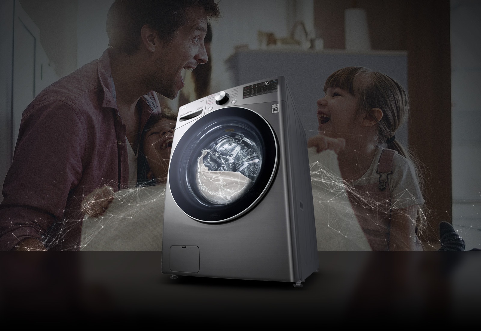 Father and daughters laugh in the background as they hold a clean blanket. A White washing machine front load washer in the foreground.