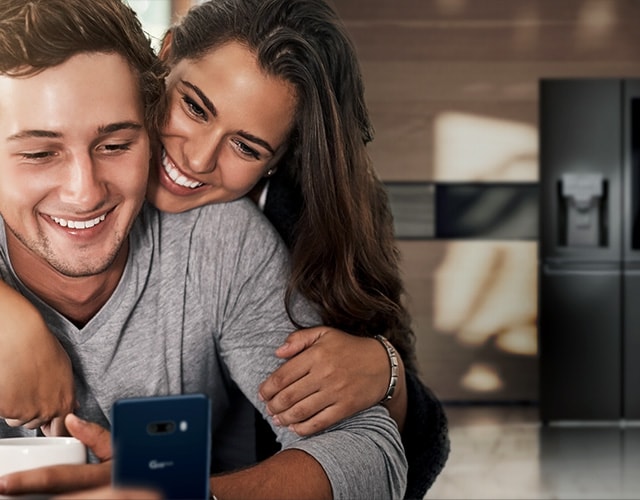A couple is looking into a smartphone with a bright smile in the kitchen.
