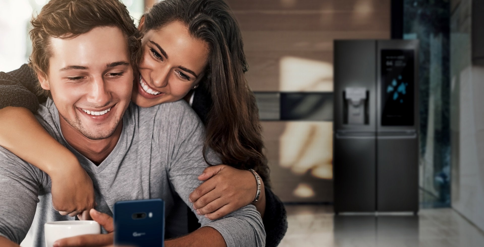 A couple is looking into a smartphone with a bright smile in the kitchen.