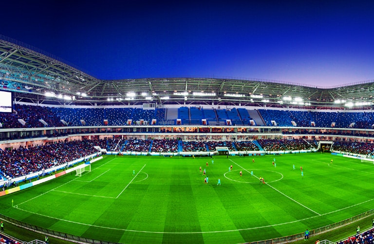 A wide-angled view of a football stadium with a full crowd and match in progress.